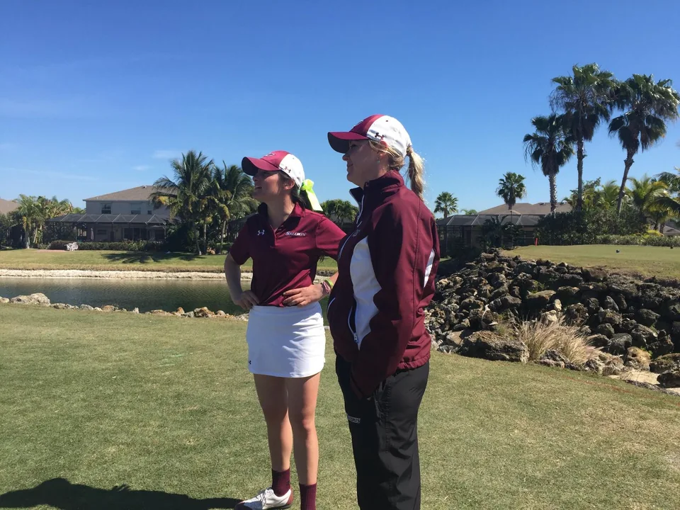 A coach and collegiate golfer together on the golf course.